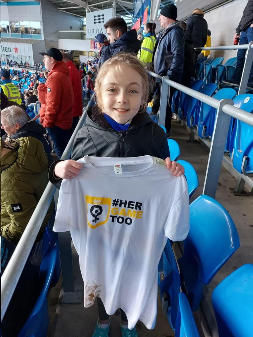 Jeune supportrice tenant un t-shirt blanc avec #HerGameToo.