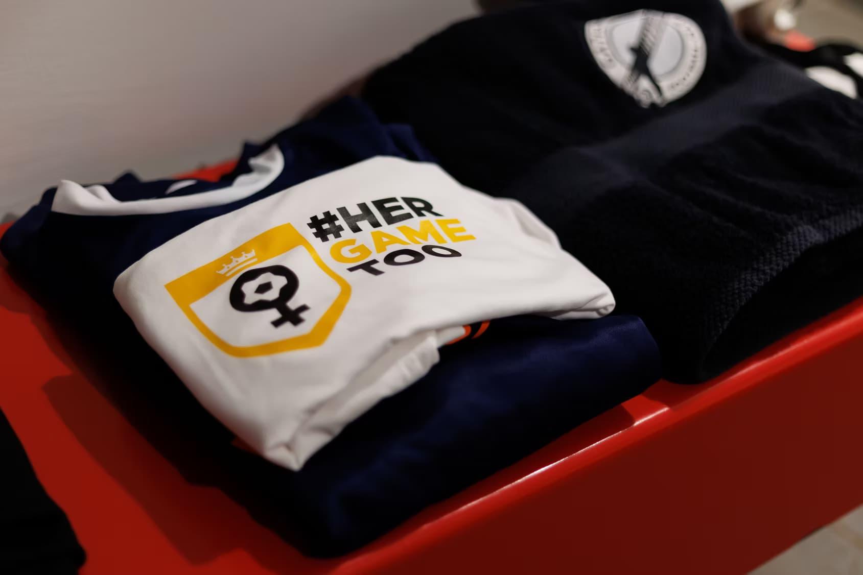 Pile de t-shirts blancs avec #HerGameToo.